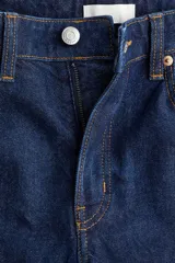 Pantalón de jean azul oscuro, de corte ancho y tobillero, con tiro alto, cinco bolsillos y cierre con botón.