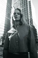 Camisa corta gris con rayas verticales blancas, cuello solapa y manga larga. Cierre frontal con botones.