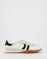 Championes deportivos de estilo retro color blanco con detalles en negro, suela fina color caramelo, capellada de cuero y nylon, lengüeta semitransparente acolchada, cordones bicolor intercambiables y cuello acolchado.