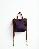 Mini cartera de cuero color morado con manijas cortas marrones, cierre con botón de madera y flecos largos laterales.