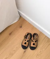 Sandalias de cuero color marrón claro, con suela de goma negra y pespuntes rojos.