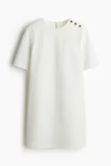 Vestido corto blanco de corte evasé, con cuello redondo y manga corta. Presenta abertura de cerradura con botón oculto en la nuca.