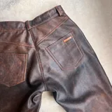 Pantalón de cuero negro, de corte recto y tiro alto, con bolsillos delanteros y traseros.