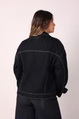 Chaqueta de denim azul oscuro, de corte holgado, con cuello clásico, cierre frontal con botones metálicos, cuatro bolsillos frontales y costuras en hilo color crudo.