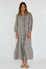 Vestido largo color beige de lino, con mangas largas abullonadas y volantes verticales en el frente. Cierre frontal con botones.