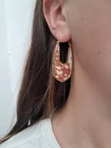 Par de aros colgantes con forma geométrica, con interior de cuero sintético negro con textura de piel de cocodrilo y borde dorado.