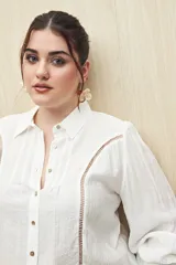Camisa blanca de manga larga con cuello clásico y botones de nácar. Presenta detalles calados en el frente.