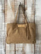 Cartera tipo tote de cuero con textura de reptil, color beige. Presenta un cierre frontal metálico dorado y un detalle de borla colgante en el mismo tono. Cuenta con doble asa de hombro.