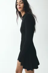 Vestido corto negro de punto con cuello redondo y manga larga. Presenta cierre frontal con cremallera metálica.