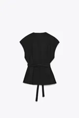 Chaleco negro cruzado con cuello solapa y sin mangas. Incluye cinturón de la misma tela para ajustar a la cintura.