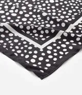 Pañuelo triangular de satén color negro con estampado de lunares blancos. Confeccionado en poliéster con acabado brillante y suave.