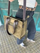 Cartera tipo tote bag de cuero color verde oliva, con doble asa corta de cuero marrón y correa larga extraíble y regulable de cuero marrón. Tiene un bolsillo frontal con cierre y un bolsillo interno.