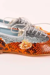 Zapato blucher de cuero con estampado animal print en tonos naranja y plateado, con cordones y detalle de borlas.