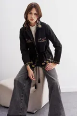 Campera negra de algodón con bordados de flores y lentejuelas. Tiene corte recto, ajuste interno en la cintura, bolsillos con solapa y cierre frontal.