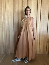 Vestido largo color ocre, sin mangas, con escote en V y bolsillos laterales. Presenta costuras verticales a lo largo del vestido.