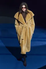 Abrigo largo color camel con efecto piel de oveja, cuello solapa, manga larga, bolsillos delanteros y cinturón ajustable con lazadas. Forro interior.