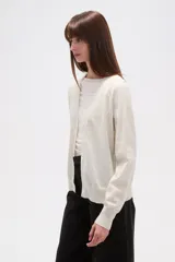 Cardigan de punto color blanco roto con motas oscuras, de manga larga y escote en V con cierre de botones frontales.