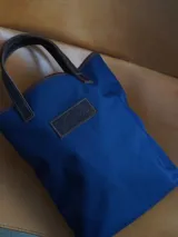 Bolso matero de lona color azul con detalles en cuero marrón, con asas cortas y logo de la marca en cuero.