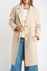 Tapado largo color beige claro, de corte oversize, con cuello solapa y cierre frontal de botones.