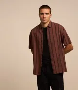 Camisa masculina de corte relajado, confeccionada en cáñamo, algodón y poliéster. Presenta cuello inglés, mangas cortas y rayas verticales texturizadas.