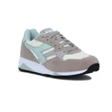 Championes deportivos Diadora modelo N902, con combinación de colores gris topo, blanco crema y detalles en verde menta claro. Presentan una construcción de paneles de gamuza y malla, entresuela blanca y suela negra.
