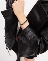 Pulsera de cuero negro con doble tira, pieza central de plata con cristal rectangular color azul y cierre de mosquetón con dije de la marca Uno de 50.