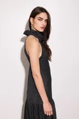 Vestido largo negro con finas líneas plateadas, de corte holgado, escote halter y espalda baja. Presenta volados en el cuello y en la cadera.