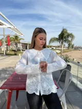 Camisa blanca de mangas largas con detalles bordados y cuello babero con puntilla.