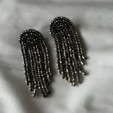 Par de caravanas colgantes con base semicircular y flecos de cuentas facetadas color gris plomo.