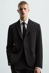 Blazer slim fit negra confeccionada en tejido con viscosa. Tiene cuello con solapas de muesca, manga larga con puño con detalle de botones, bolsillo de vivo en pecho, bolsillos de solapa en cadera, bolsillo interior, bajo con aberturas en espalda y cierre frontal con botones.