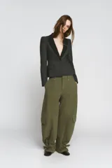 Pantalón cargo de mujer color verde militar, tiro medio, corte ancho y recto (barrel). Presenta bolsillos laterales y bolsillos de plastrón con solapa en las piernas. El bajo es ajustable con trabillas y hebillas metálicas.