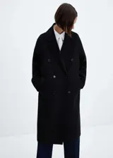 Abrigo largo negro oversize con doble botonadura, solapas con muesca, hombros caídos, bolsillos laterales y abertura posterior.