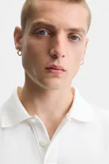 Polo blanco de piqué con corte relaxed fit, cuello solapa y cierre frontal con botones.