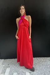 Vestido largo strapless con corpiño fruncido en color fucsia brillante y falda amplia en color rojo vibrante. La prenda tiene bolsillos laterales.