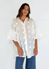 Camisa blanca con lunares blancos en relieve, cuello clásico, cierre frontal con botones y mangas 3/4 con volados.