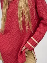 Sweater color crema con tejido en ochos, cuello redondo, puños acanalados con doble raya azul y tajos a los costados.