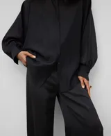 Camisa blanca de manga larga, con cuello chimenea alto y botonadura frontal oculta. El tejido es semitransparente y presenta una textura ligera.