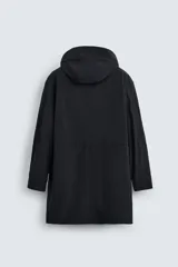 Parka negra de tejido técnico ligero, corte regular, cuello alto con capucha ajustable, manga larga con puños ajustables, cintura ajustable con cordón interno, bolsillos de solapa en la cadera, abertura en la espalda y cierre frontal con cremallera oculta y botones a presión.