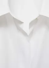 Camisa blanca oversize de algodón orgánico, con cuello camisero, manga larga con puños abotonados, bolsillo de parche en el pecho y cierre frontal con botones.