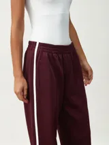 Pantalón deportivo color borgoña, de corte ancho y cintura elástica. Presenta una franja blanca vertical a lo largo de la pierna.