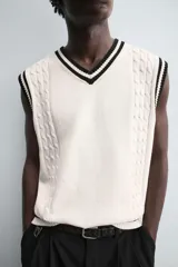 Chaleco de punto color crema con cuello en pico y ribetes negros en cuello, sisas y bajo.