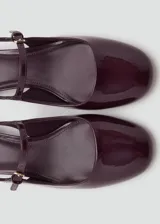 Zapato destalonado de efecto charol color borgoña, con tacón bloque de 3 cm y puntera redondeada. Posee una tira fina ajustable con hebilla sobre el empeine.