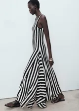 Vestido largo de punto fino, con tirantes anchos y cuello caja. Presenta un estampado de rayas verticales en blanco y negro, y un bajo asimétrico.