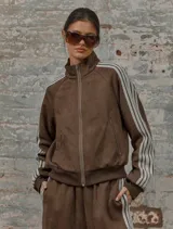 Conjunto deportivo marrón de dos piezas: campera con cremallera, cuello alto, mangas largas con puño y detalles de rayas blancas en mangas y laterales del pantalón. Pantalón recto de cintura alta con cordón ajustable.
