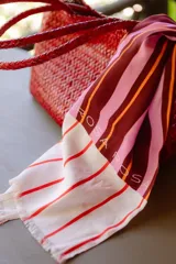 Pareo rectangular de viscosa con estampado de rayas verticales en tonos rosa, marrón y naranja. Tiene flecos en los extremos y el logo de la marca en una esquina.