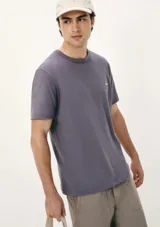 Remera gris con cuello redondo y manga corta. Presenta un pequeño parche con logo en el pecho.