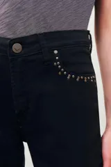 Pantalón jean negro de corte slim con detalles de tachas plateadas en los bolsillos delanteros y en el ruedo.