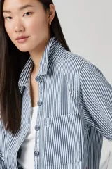 Camisa a rayas verticales azules y blancas, con cuello clásico, cierre frontal con botones y dos bolsillos de parche en el pecho.