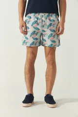 Short de baño estampado con hojas de palmera en tonos azul y verde. Tiene cintura elástica con cordón ajustable, dos bolsillos laterales y uno trasero.