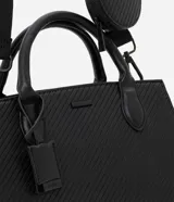 Cartera satchel negra de material sintético con textura diagonal, doble asa de mano y asa larga removible de gross. Incluye porta monedas y cierre por cremallera.